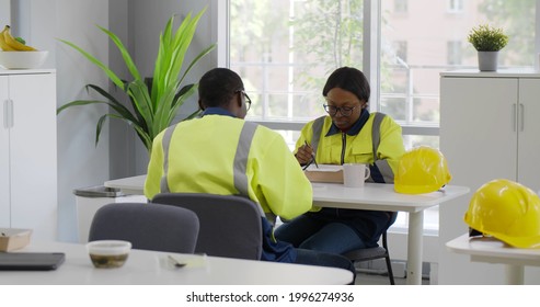 African Warehouse Workers Eating Meal In Industrial Canteen. Multiethnic Industrial Employees Relaxing And Having Lunch In Office Or Cafeteria