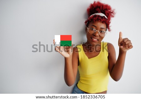 African woman with afro hair, wear yellow singlet and eyeglasses, hold Madagascar flag isolated on white background, show thumb up.