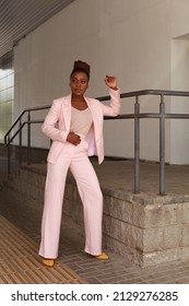 African Woman With Afro Hair Wearing Pink Summer Suit  Posing Outside At Urban Minimalist Background. Glamorous And Modern Style Runaway Full Length Portrait. Modeling And 2022 Fashion Concept.