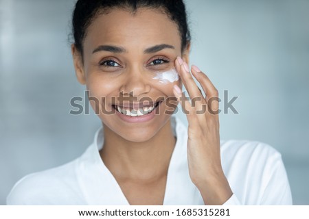 African woman apply day creme close up female attractive happy face. Using facial cream after 30s to keep skin collagen and elastin rate, hydrate and nourish it. Beauty treatment and skincare concept