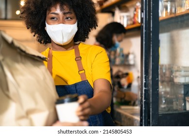 African Woman Barista  Wear Mask Due To Covid-19 Pandemic, Receive Drink On Coffee Bar Counter. Restaurant Worker Giving Takeaway Delivery Food Bag.Small Business Social Distance Concept.