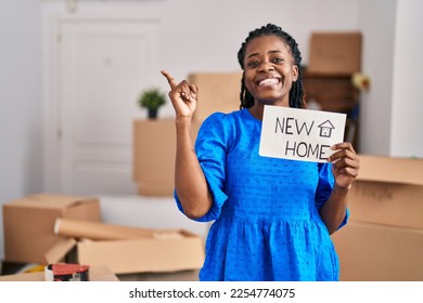 African woman with braided hair moving to a new home holding banner smiling happy pointing with hand and finger to the side  - Shutterstock ID 2254774075