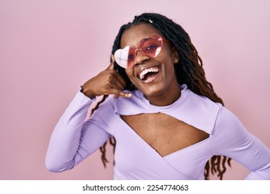 African woman with braided hair standing over pink background smiling doing phone gesture with hand and fingers like talking on the telephone. communicating concepts.  - Shutterstock ID 2254774063