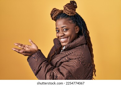 African woman with braided hair standing over yellow background pointing aside with hands open palms showing copy space, presenting advertisement smiling excited happy  - Shutterstock ID 2254774067