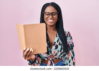 African woman with braids reading a book looking positive and happy standing and smiling with a confident smile showing teeth  - Shutterstock ID 2230603533
