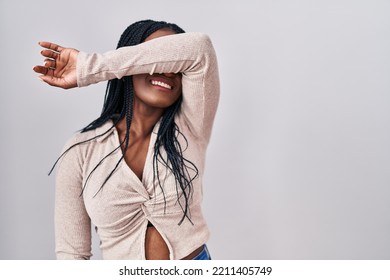 African Woman With Braids Standing Over White Background Covering Eyes With Arm Smiling Cheerful And Funny. Blind Concept. 