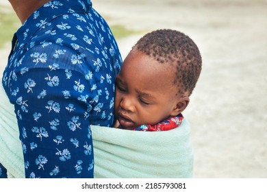 African Woman Carries Her Asleep Child Wrapped In A Towel In Her Back In A Traditional Way