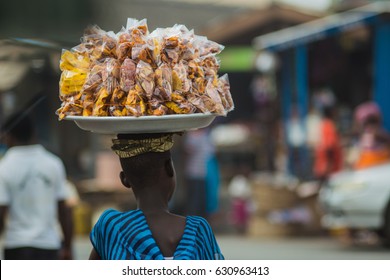 African woman carrying plantain and cassava chips on her head as she walks through a market in Cape Coast, Ghana	
