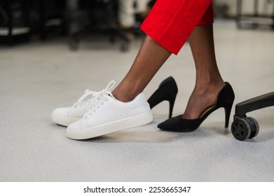 African woman changing from high heels to sneakers in the office. Tired legs. 