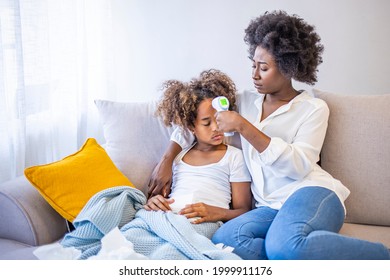 African Woman Checking Temperature With Hand Of Little Ill Daughter. Mother Checking Temperature Of Her Sick Indian Girl. Sick Child Lying On Bed Under Blanket With Woman Checking Fever On Forehead