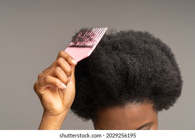 African woman combing curly hair. Cropped image of ethnic female hand holding hairbrush at head with wavy afro hairdo. Haircare equipment for ethnic hairstyle. Care and beauty for mixed race concept