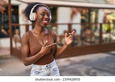 African woman with curly hair outdoors at the city wearing headphones afraid and shocked with surprise and amazed expression, fear and excited face.  - Shutterstock ID 2199428935