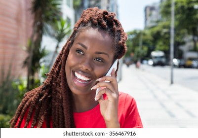 African woman with dreadlocks laughing at phone in the city