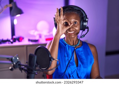 African woman with dreadlocks wearing headphones smiling happy doing ok sign with hand on eye looking through fingers  - Shutterstock ID 2326293347