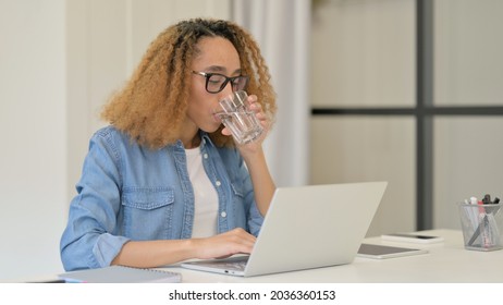 African Woman Drinking Water while working on Laptop 
