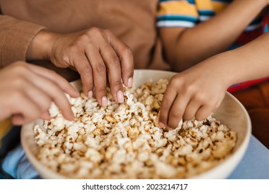 African woman eating popcorn with her children sitting on a couch at home