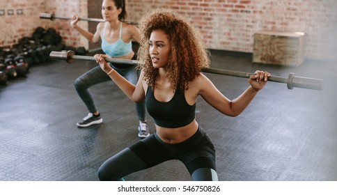African woman exercising with barbell in fitness class. Female workout in gym with barbell.