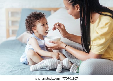 African woman giving her baby to eat and sitting in bedroom.