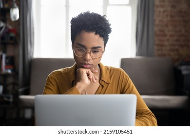 African woman in glasses sit at desk staring at laptop screen, learn new software, makes assignment, working looks concentrated, search solution or ideas. Business challenge, thinks over task concept
