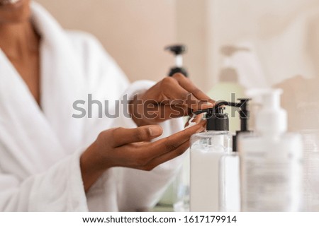 African woman hands using cosmetic liquid soap in bathroom. Close up of girl black hands in bath robe using body lotion dispenser after shower. Black girl putting pomade on hand from pump.