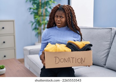 African woman holding donations box for charity in shock face, looking skeptical and sarcastic, surprised with open mouth  - Shutterstock ID 2265553543