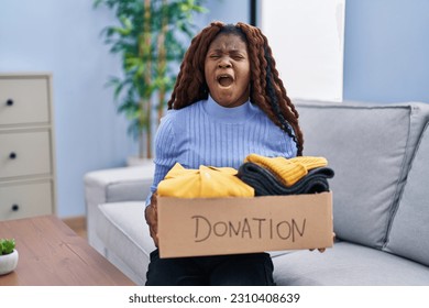African woman holding donations box for charity angry and mad screaming frustrated and furious, shouting with anger looking up.  - Shutterstock ID 2310408639