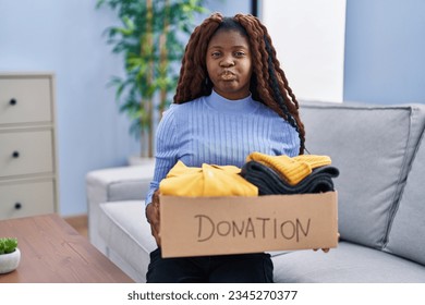 African woman holding donations box for charity puffing cheeks with funny face. mouth inflated with air, catching air.  - Shutterstock ID 2345270377