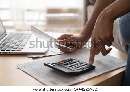 African woman holding paper bills using calculator, close up vie