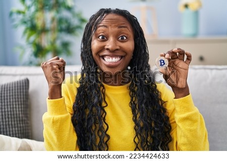 African woman holding virtual currency bitcoin screaming proud, celebrating victory and success very excited with raised arms 