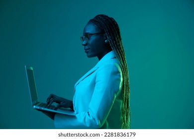 African African woman with laptop in glasses on a blue background in neon light, color mixed light. Data storage cyber security, hacker, big data. - Powered by Shutterstock