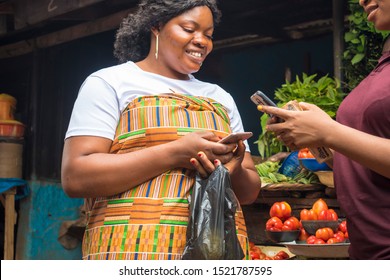 African Woman In A Local Market Doing Money Transfer For A Trader With Her Mobile Phone