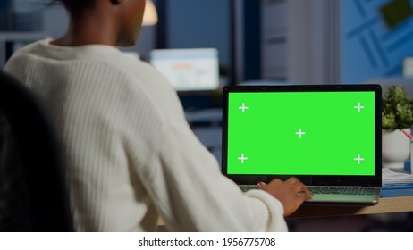 African Woman Manager Looking At Mock Up Monitor Of Laptop, Green Screen Mockup, Chroma Key Desktop Sitting At Desk In Business Office Late At Night. Freelancer Watching At Isolated Desktop Overwork