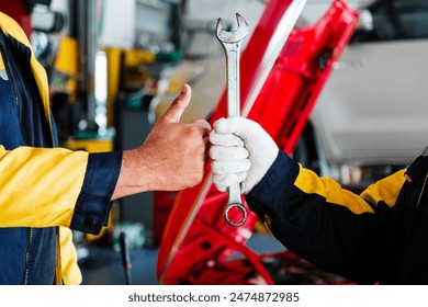 African woman mechanic holding wrench fist bunp with Indian man mechanic thumbs up with blur garage in the background. Auto car repair service center. Professional service. Vehicle maintenance. - Powered by Shutterstock