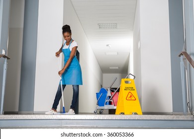African Woman Mopping Corridor Besides Caution Sign