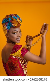 African woman in national clothes and with a headscarf. She is holding jewelry in her hands.