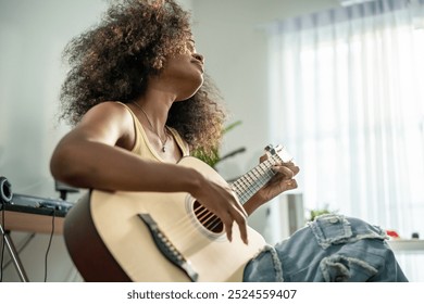 African woman play guitar and produce electronic soundtrack at home. Attractive female pianist artist musician composing, create new song on midi piano and audio equipment in recording music studio. - Powered by Shutterstock