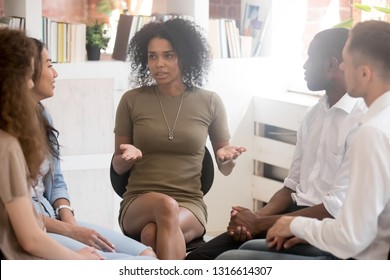 African woman psychologist coach speaking at diverse team training or group therapy session, black female trainer counseling addicted people or employees talking sharing problems sitting in circle