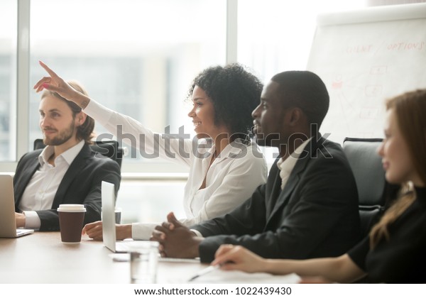 African woman raising hand to ask question\
at team training, curious black employee or conference seminar\
participant vote as volunteer at group office meeting with\
multiracial diverse\
businesspeople
