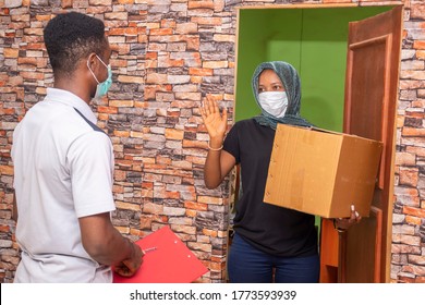 african woman receiving a parcel from a delivery service worker, wearing a face mask, waves the courier