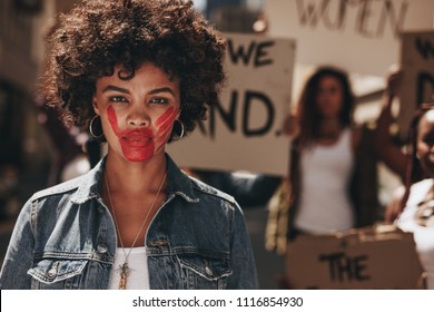 African Woman With Red Colored Hand On Her Mouth During A Protest. Group Of Female Activist Demonstrating To Stop Women Abuse.