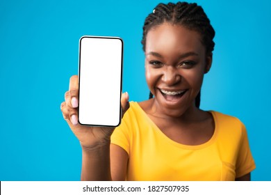 African Woman Showing Phone Blank Screen Smiling To Camera Recommending Mobile Application On Blue Studio Background. Smartphone Empty Display For Cellphone App Advertisement. Selective Focus, Mockup