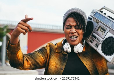 African woman singing and listening music from vintage boombox stereo with city in background - Focus on face