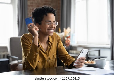 African woman sit at desk hold credit card use smartphone do on-line shopping. Happy user of e-commerce retail services, quick money transfer, buy goods on internet, secure payment via e-bank concept Foto Stock