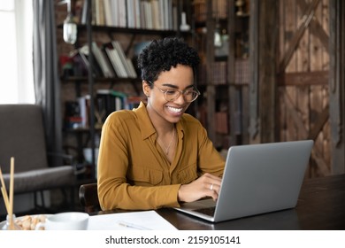 African woman sit at desk working on laptop, student studying makes assignment looks happy, feels satisfied. Workflow use modern tech, chat on-line, share messages with friends in social media concept