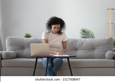 African Woman Sit On Sofa At Coffee Table Holding Pen Writing Working From Home, Noting Writing Down, Housewife Planning Week Write To-do List, Student Learning Preparing University Admission Concept