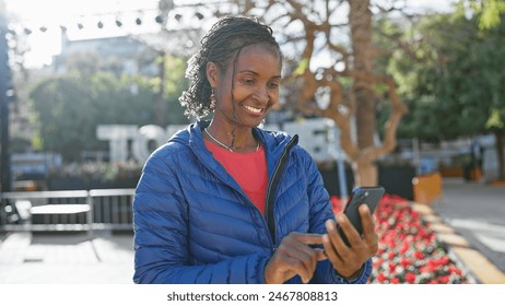 African woman smiling while using smartphone on sunny urban street.