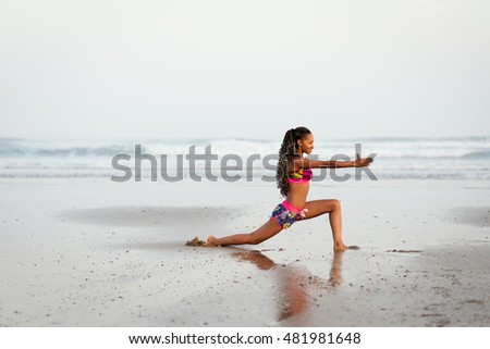African woman stretching legs in yoga pose at the beach. Sporty fit female dancer exercising against the sea.