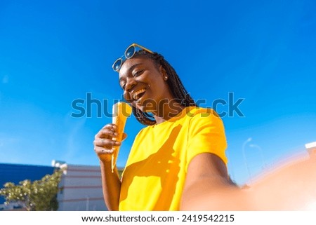 African woman taking a selfie while eating ice cream outdoors in the city in a sunny day