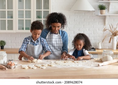 African woman teach little adorable children cooking homemade cookies, using dough shaper cutters, making preparing biscuits together in modern kitchen. Hobby, kids development, share skill concept - Powered by Shutterstock