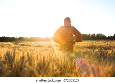 African Woman In Traditional Clothes Standing In A Field Of Barley Or Wheat Crops At Sunset Or Sunrise